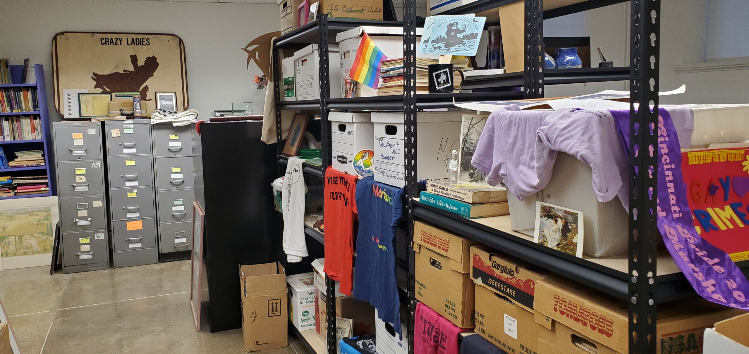 Photograph of interior of Ohio Lesbian Archives with boxes, file cabinets, t-shirts, posters, and ephemera.